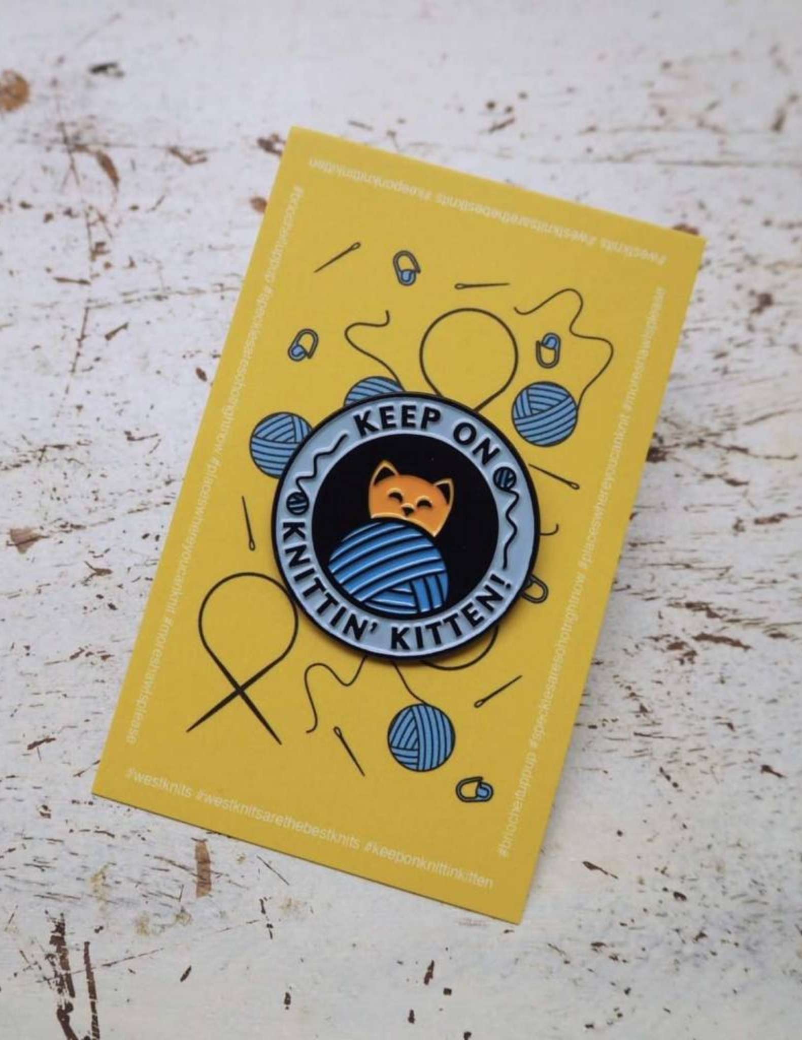 An enamel pin saying 'keep on knittin' kitten' showing a cat and a ball of yarn
