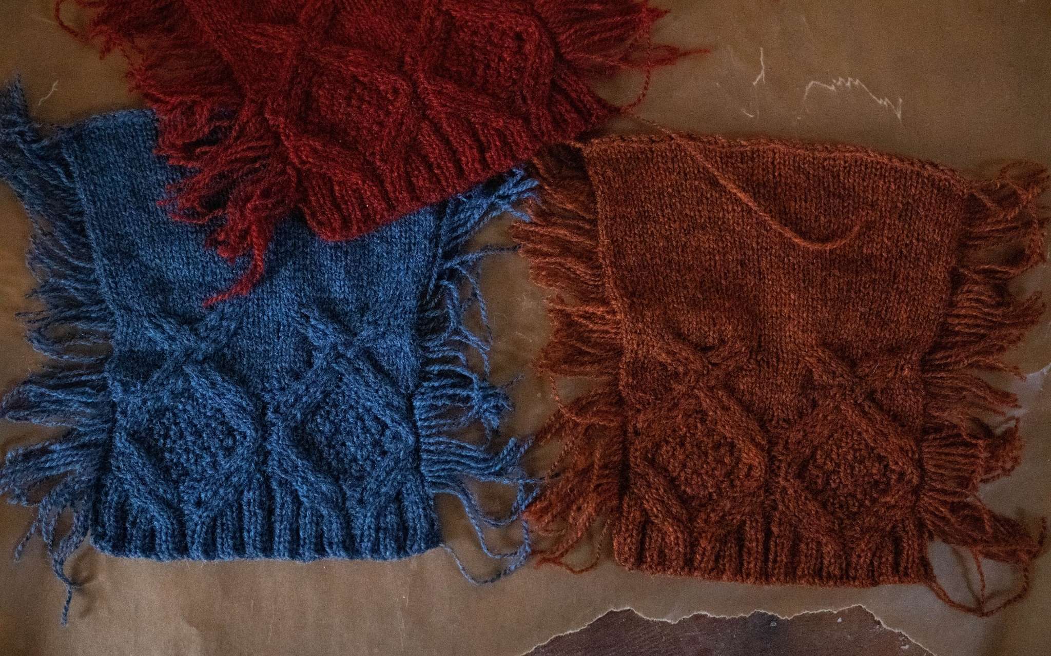 Blue and orange cabled swatches lie next to each other on a flat surface, with a red cabled swatch overlapping slightly at the top.