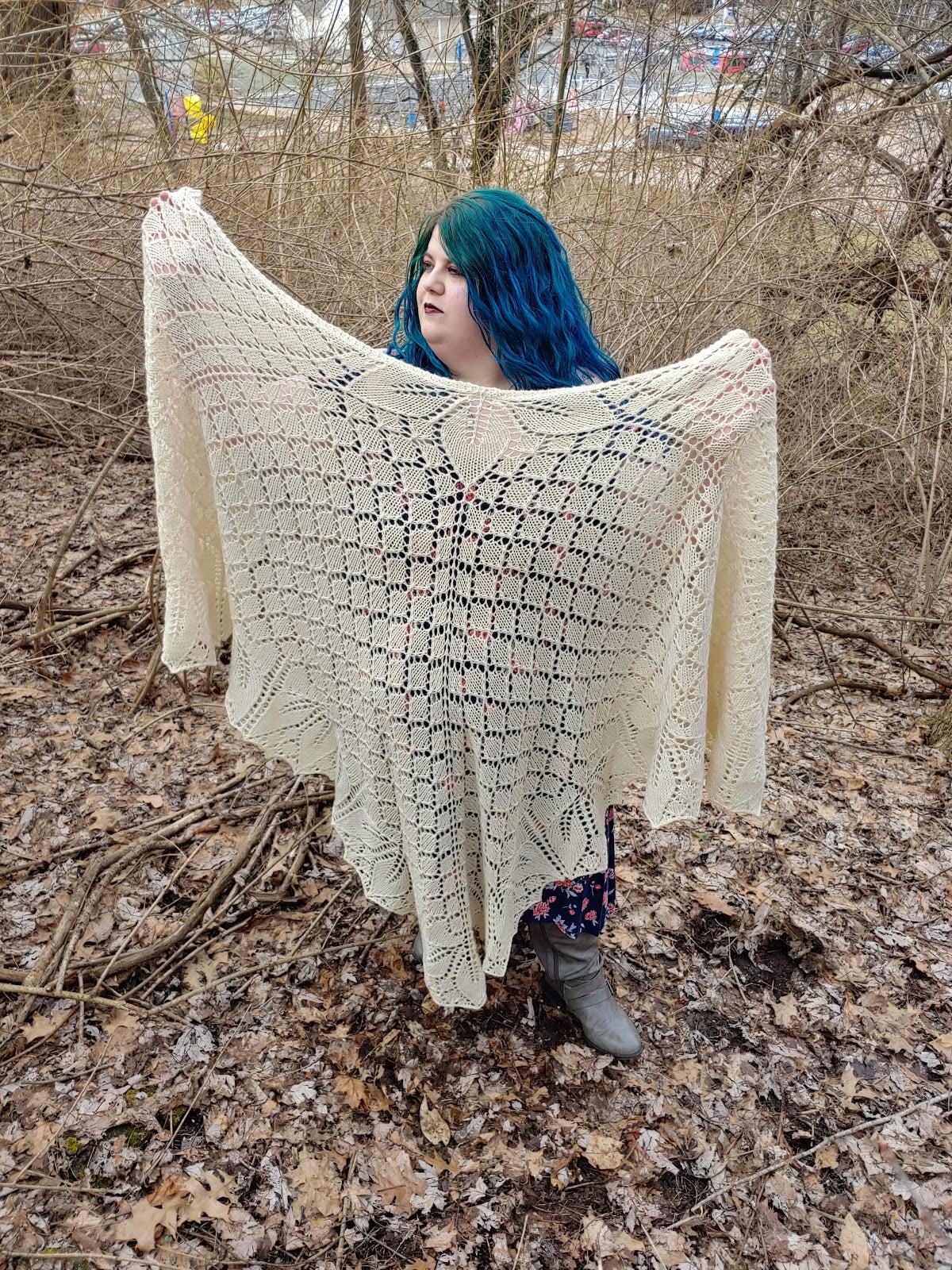 A white woman in a purple flora dress with long blue hair stands in a autumnal forest. She is facing the camera with her arms outstretched showing how large her Orchid Thief cape is, it is wider than her armspan and nearly reaches the ground.