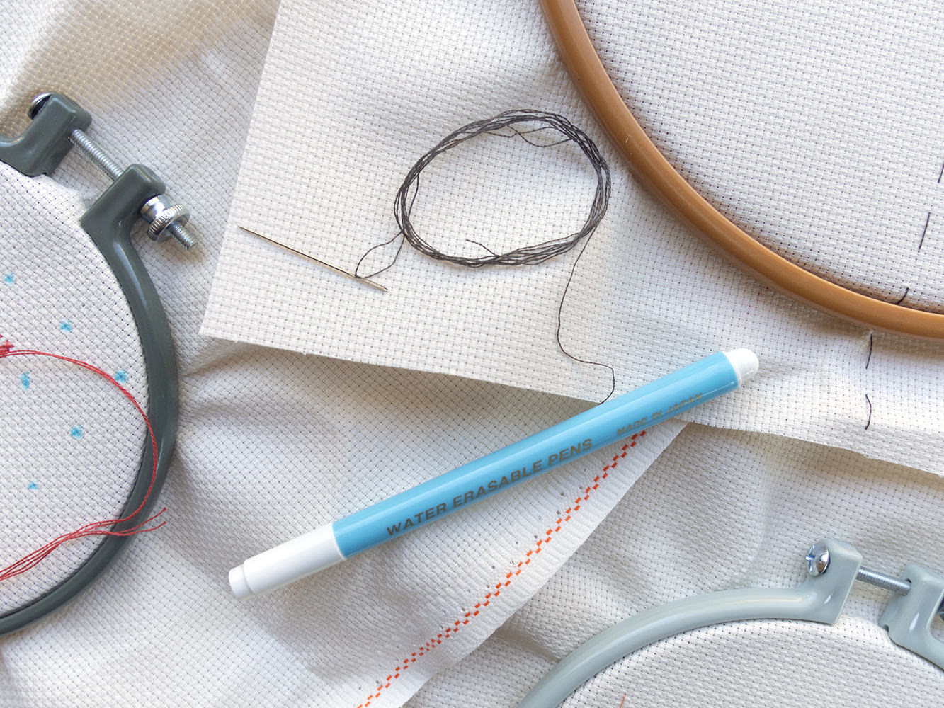 embroidery hoops, aida fabric and a water soluble marker. One of the hoops has fabric marked with a grid of dots in it.
