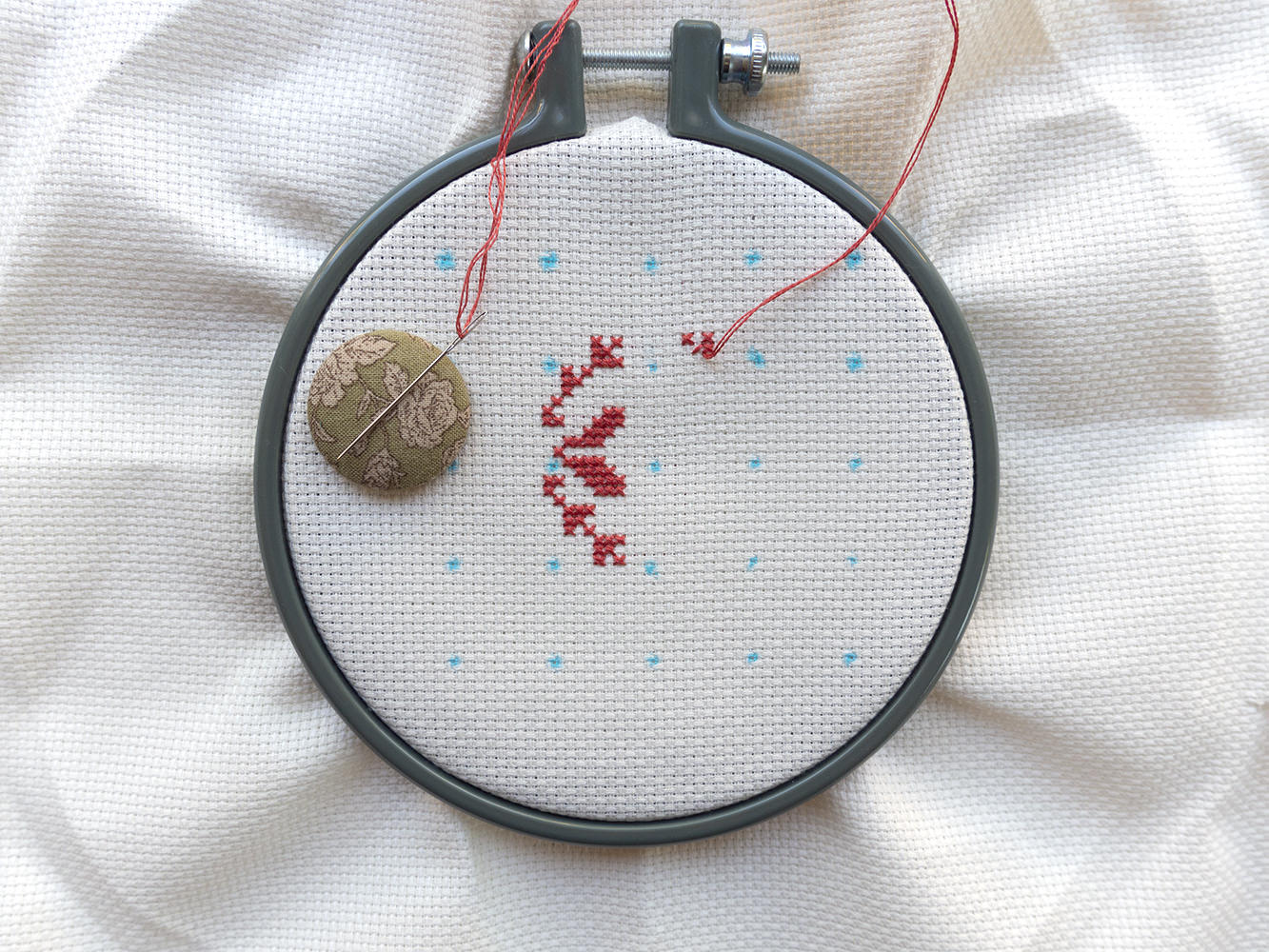 part of a snowflake stitched on dot marked aida in a small hoop 