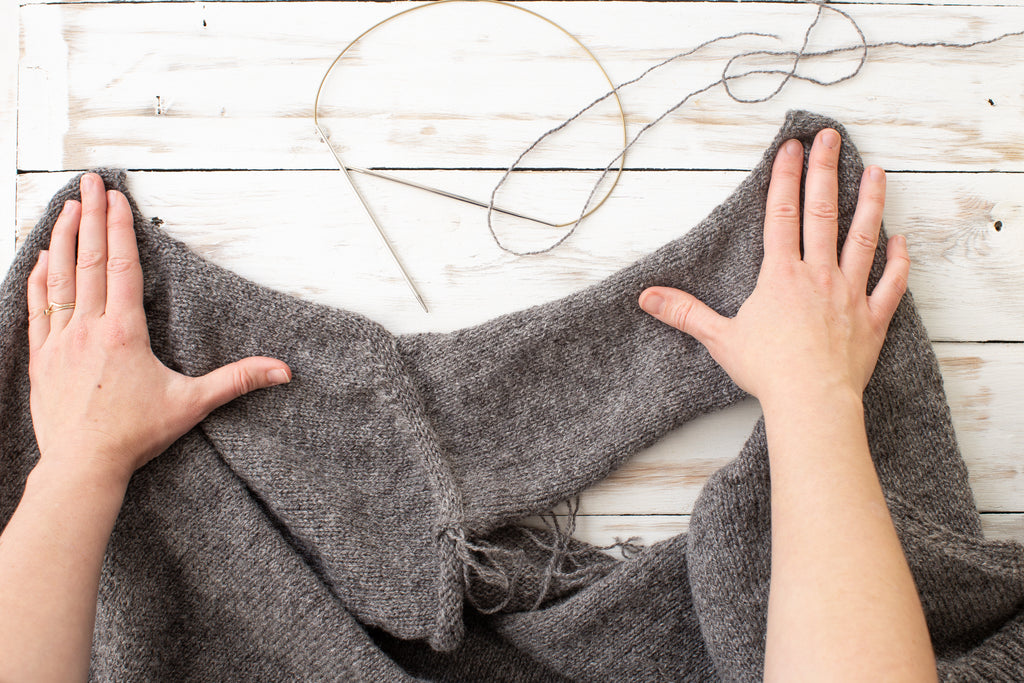 Image of a pair of white skinned hands holding the cardigan pieces flat.