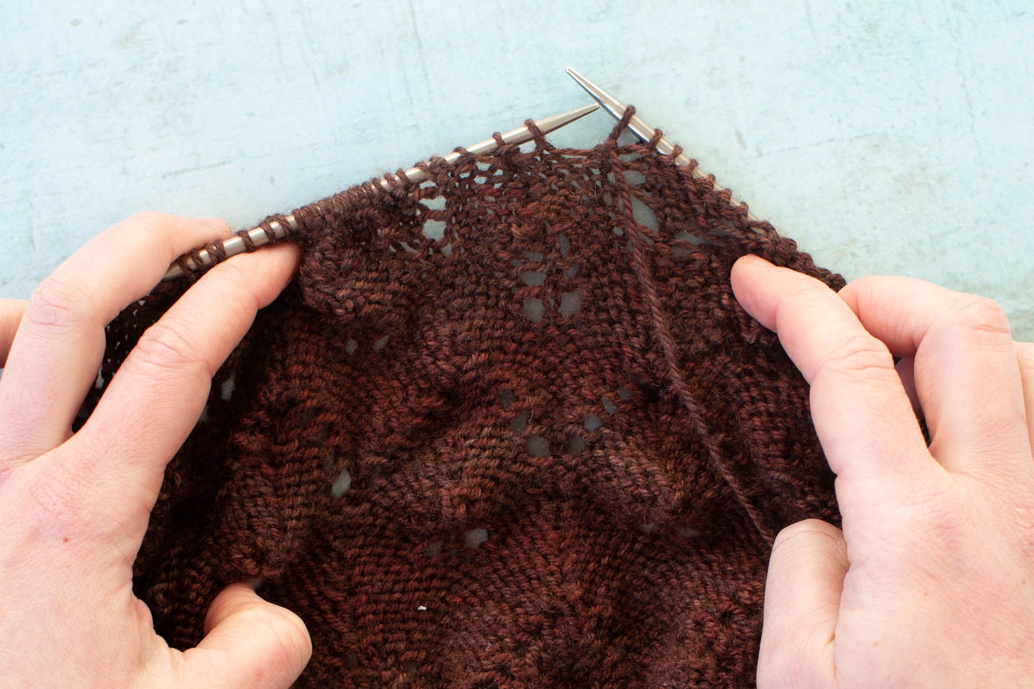 a brown shawl is being spread out on the needles with the wrong side facing