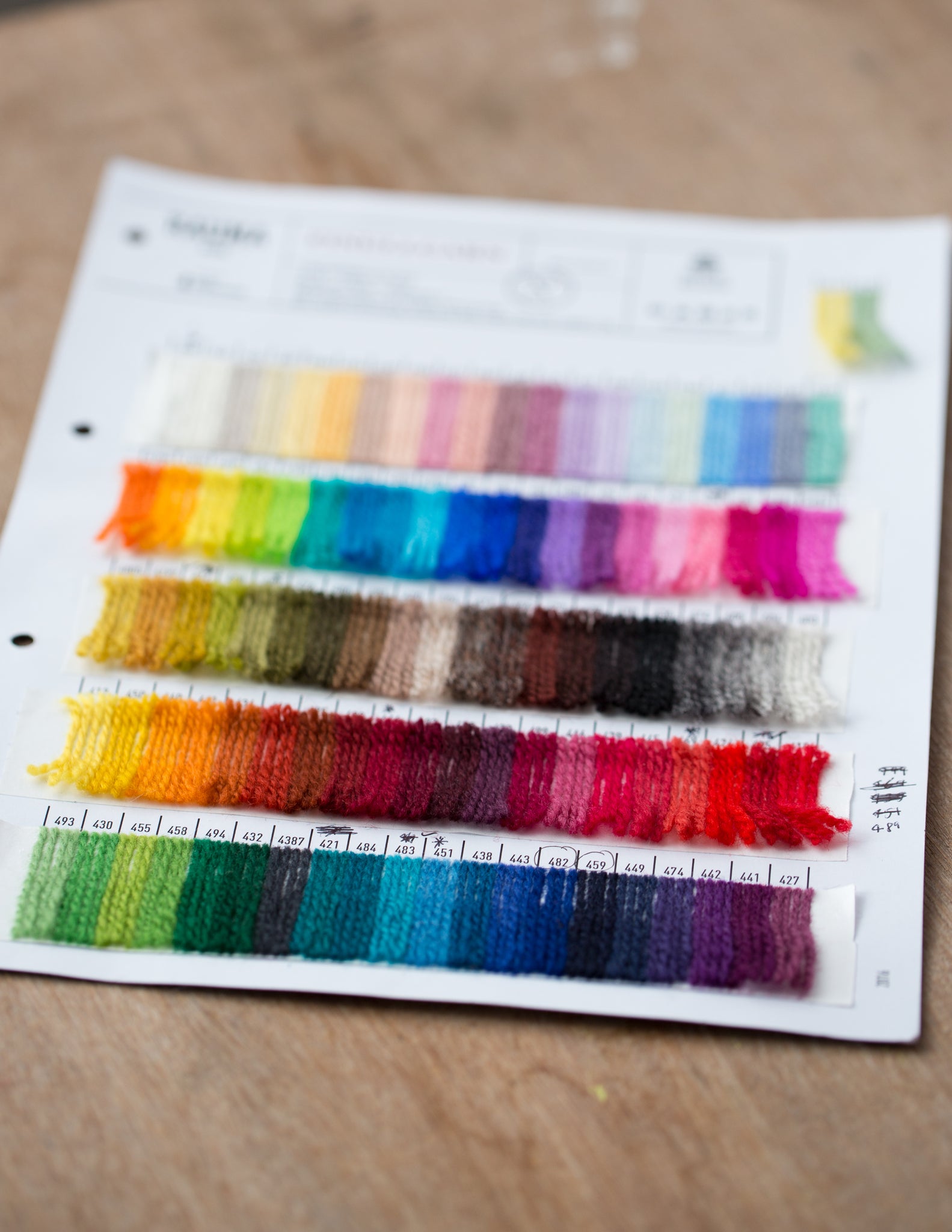 a shade card showing a rainbow of colours lays on a wooden surface