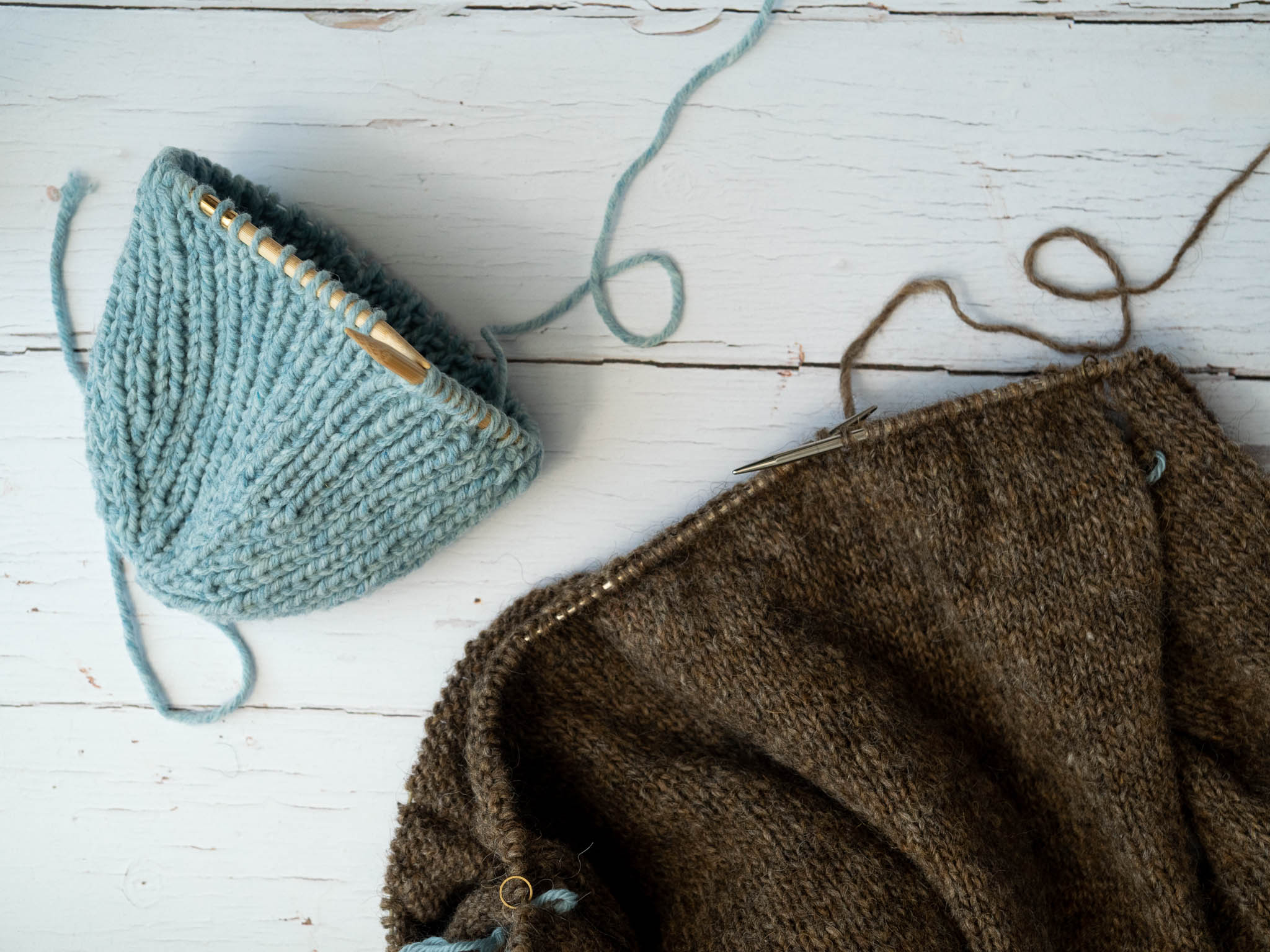 a brown sweater and a blue hat in progress pictured on a white wooden background