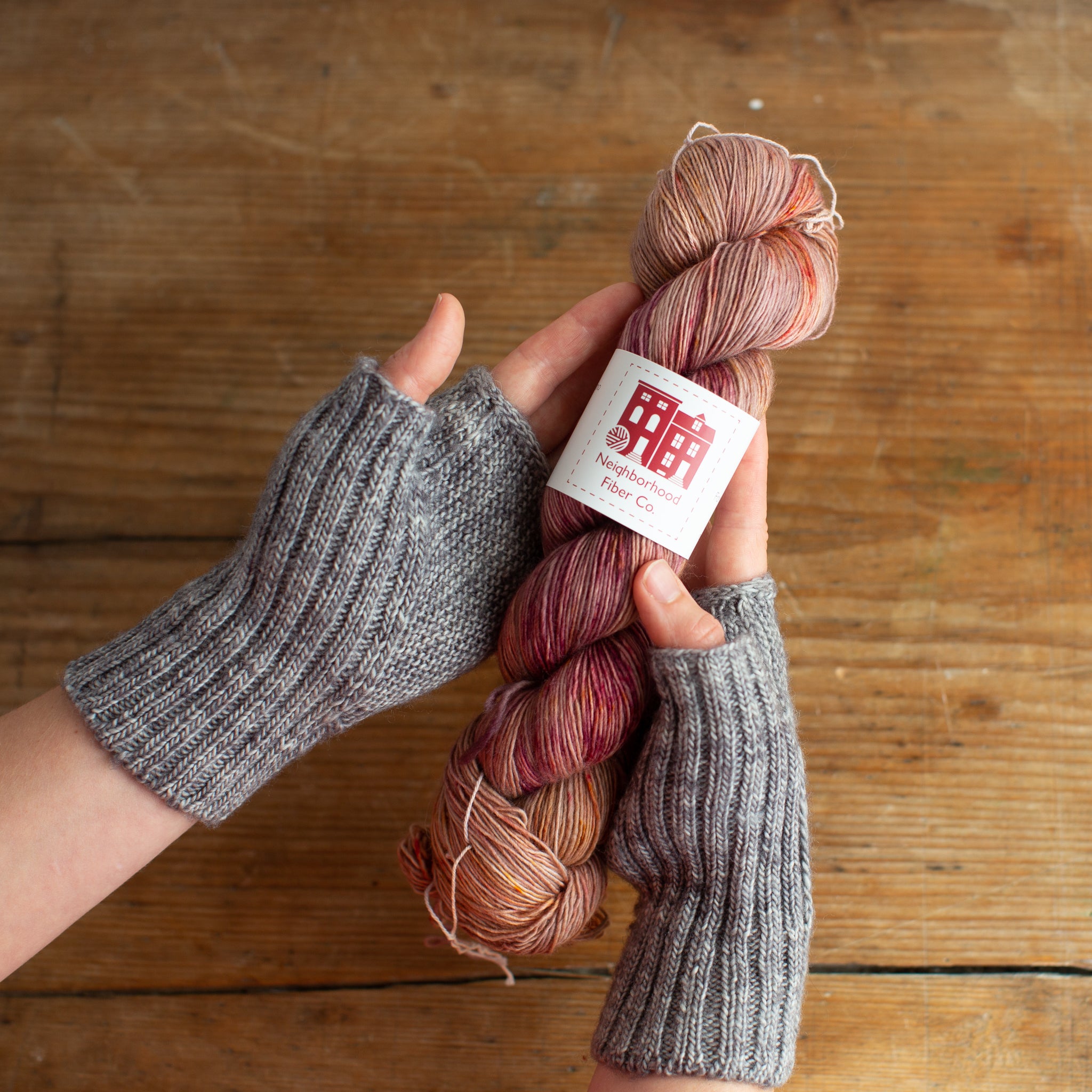 Ysolda wearing grey Kaerlig mitts and holding a skein of Neighborhood Fiber Co. Rustic Fingering in softly variegated earthy pinks