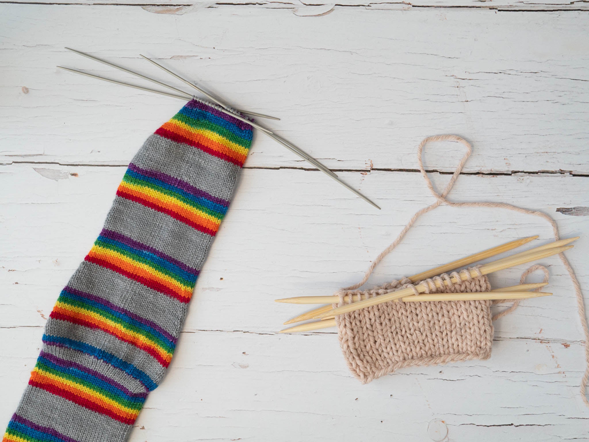 a rainbow striped sock and a small pink swatch both on double pointed needles