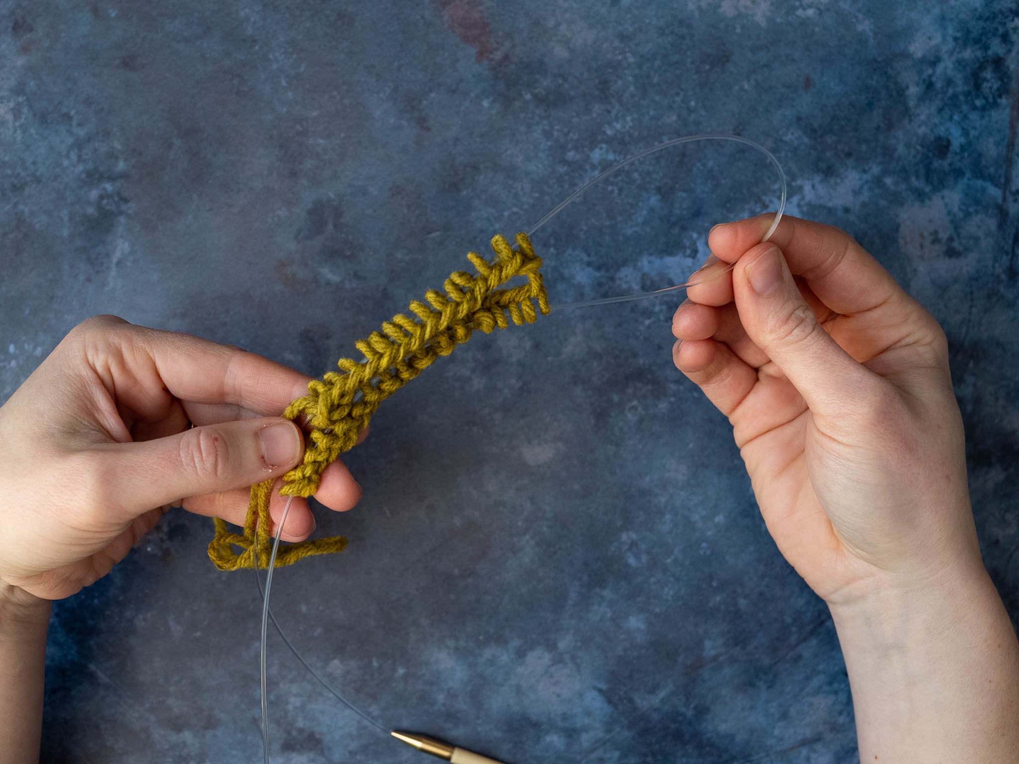 a loop of cable pulled out to the right halfway along the cast on stitches, which are all on the cables