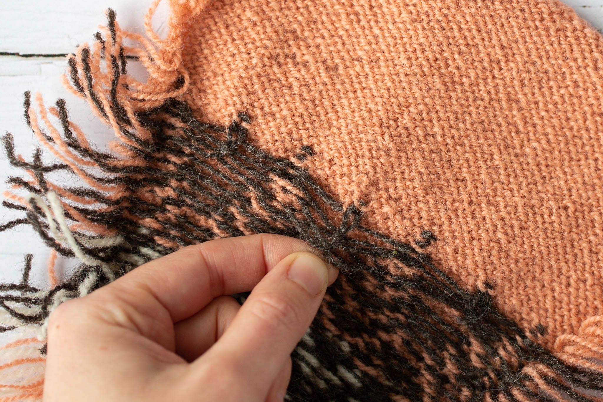 The reverse side of a coral and brown coloured piece of knitting, a hand holds one of the brown strands on the knitted fabric