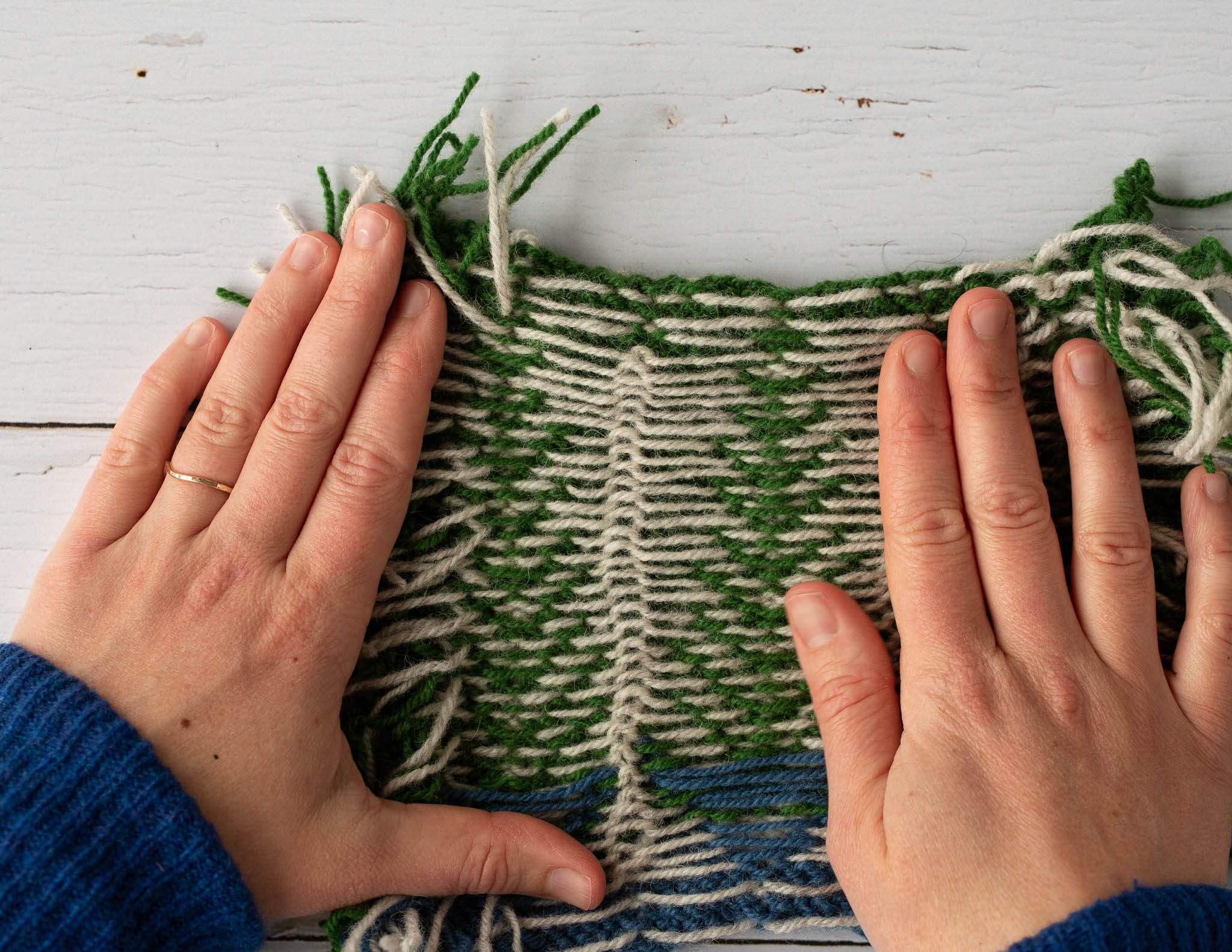 two white hands hold a piece of knitting flat, showing the reverse with long white floats of yarn set on top of a green main colour