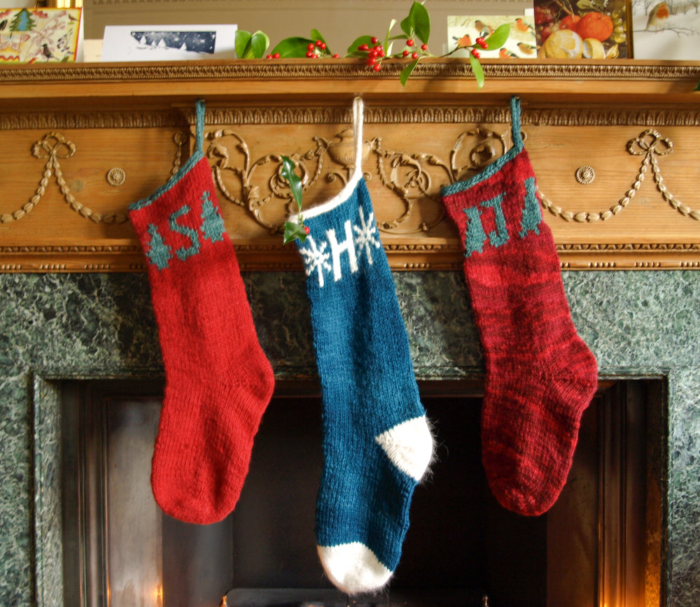 3 knitted Christmas stockings in red, green and teal hanging from a mantelpiece