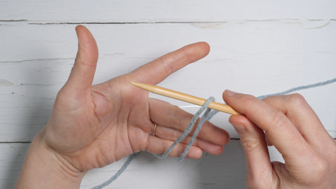 both strands are in front of the left hand, which is held with the palm open and index finger and thumb at the top