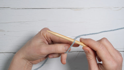 the yarn is gripped in the left hand, with the index finger and thumb being inserted between the two strands