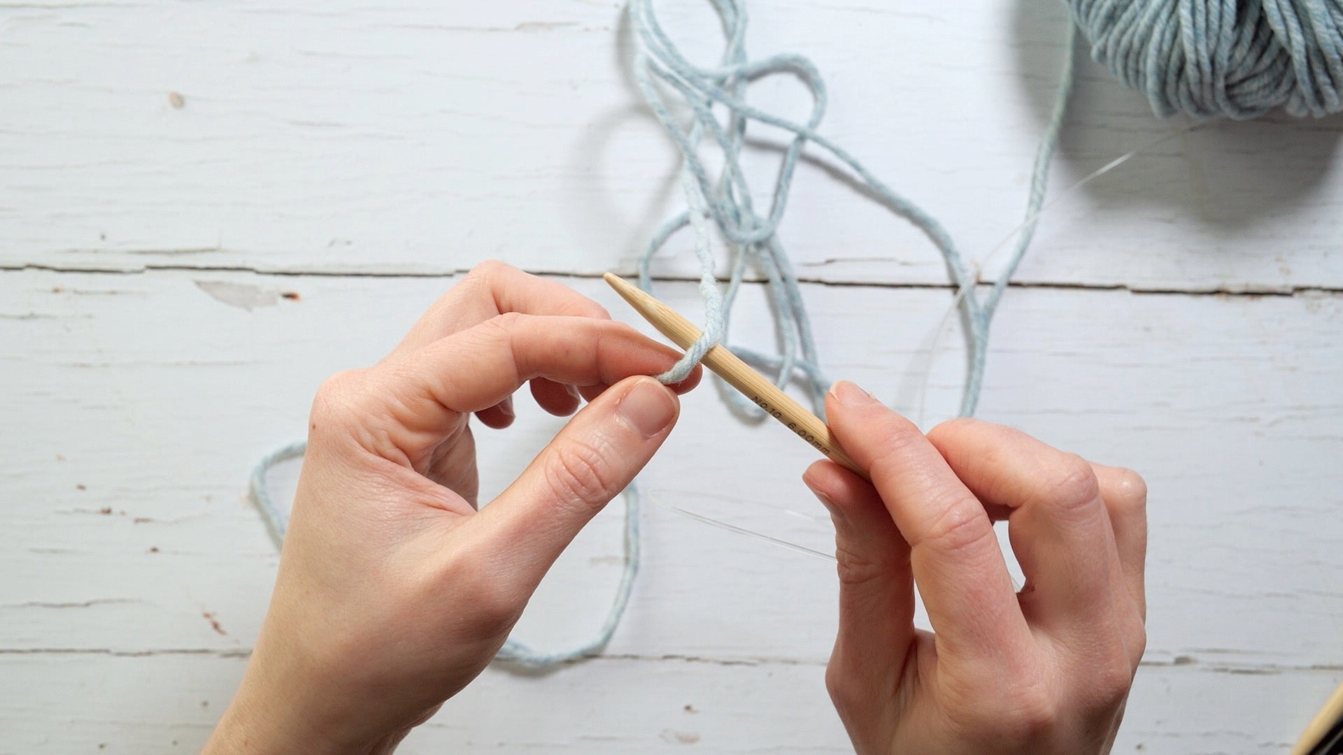 a knitting needle is held in the right hand, with the yarn draped over it