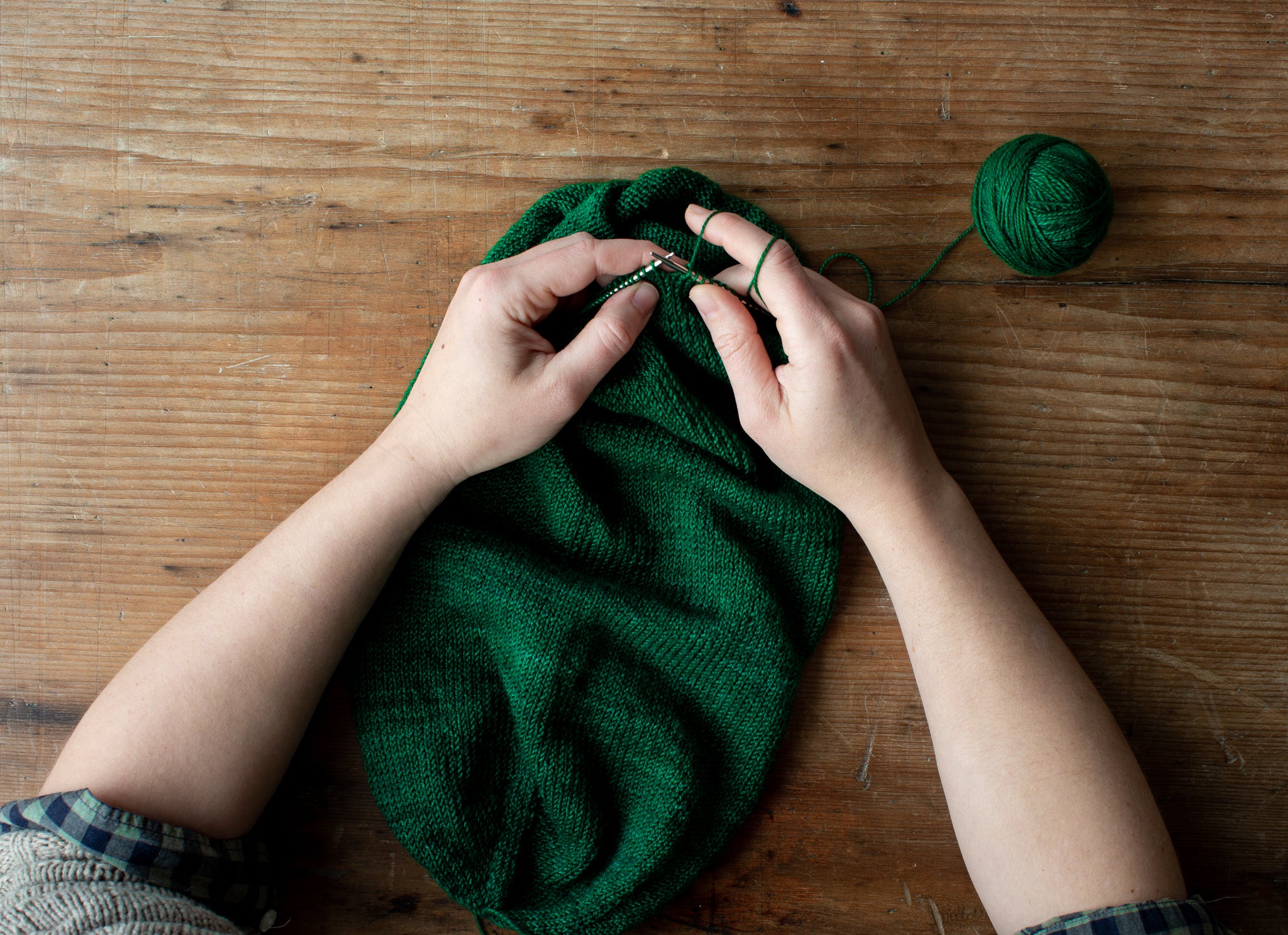 someone knitting a dark green project in the round on a circular needle