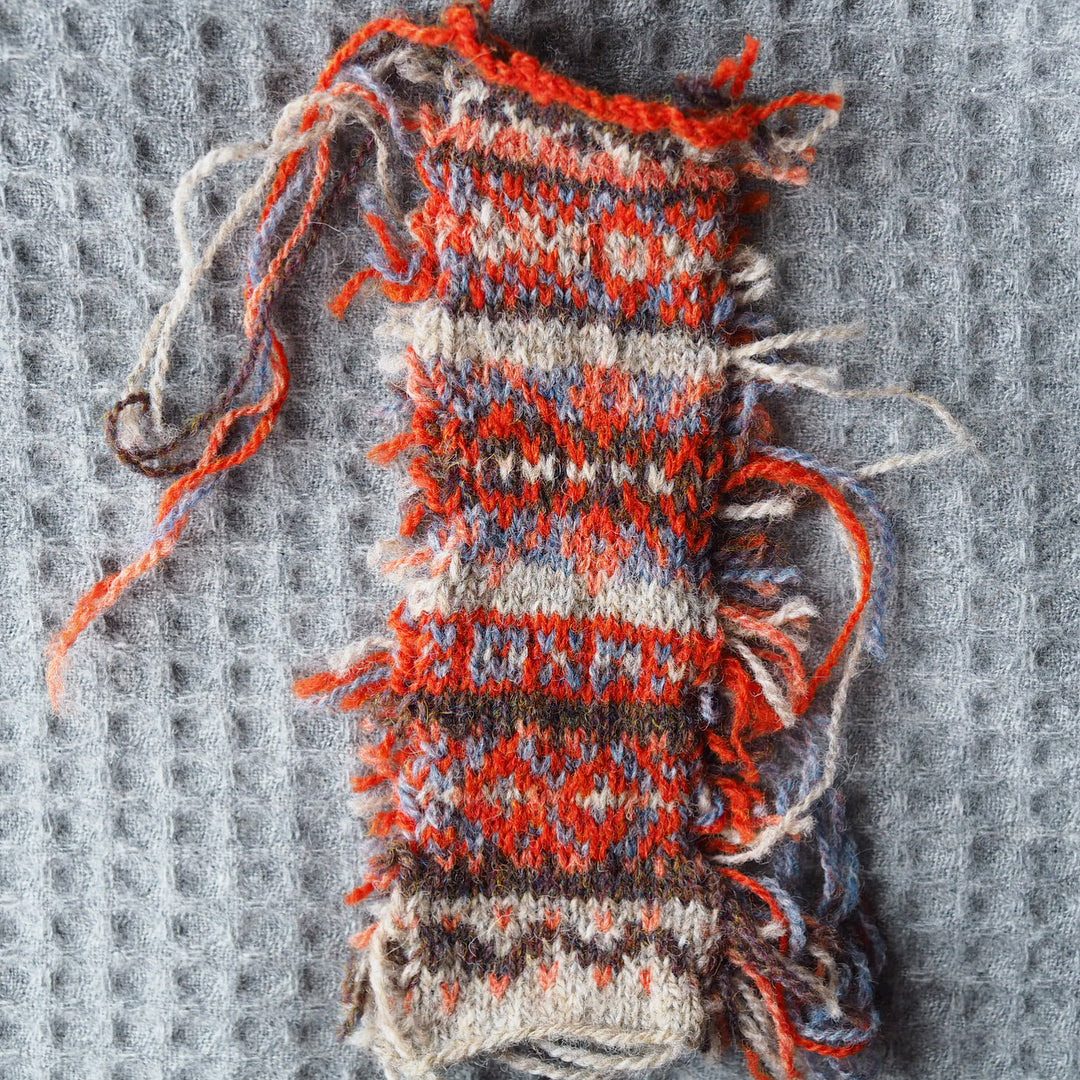 Image is of a colourwork swatch in shades of orange and purple - different combinations are tried out as the swatch progresses.