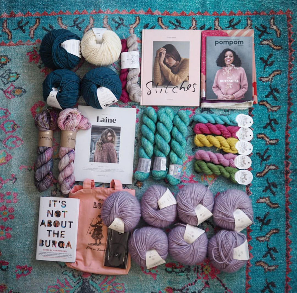 Thebrightblooms's EYF Purchases: Balls and skeins of yarn arranged in a blue patterned carpet. Copies of Pompom, Laine, Stitches and It's Not About the Burqa are arranged among the yarn.