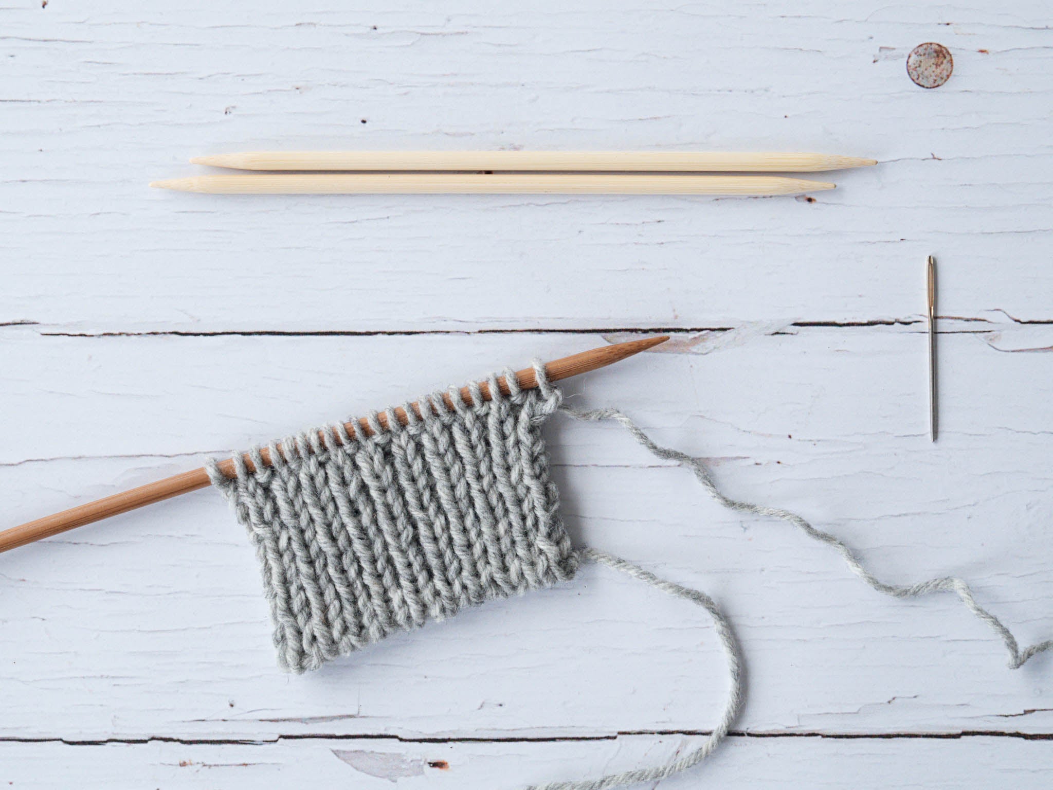 ribbed swatch on a wooden needle with two dpns and a darning needle