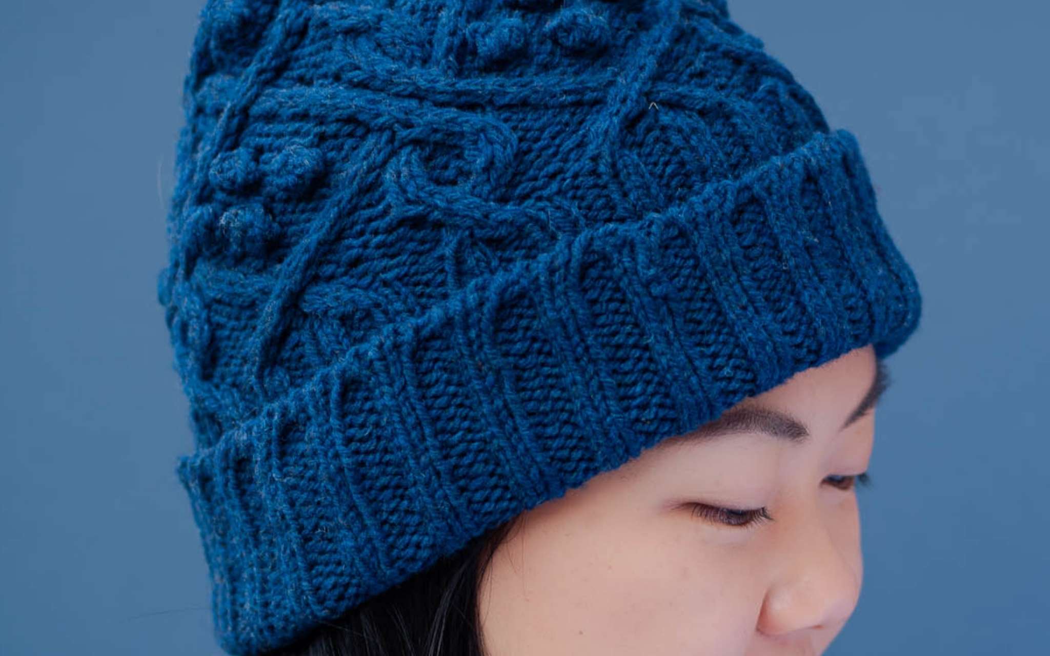 a close up of the brim of a blue cabled hat with a ribbed, folded edge