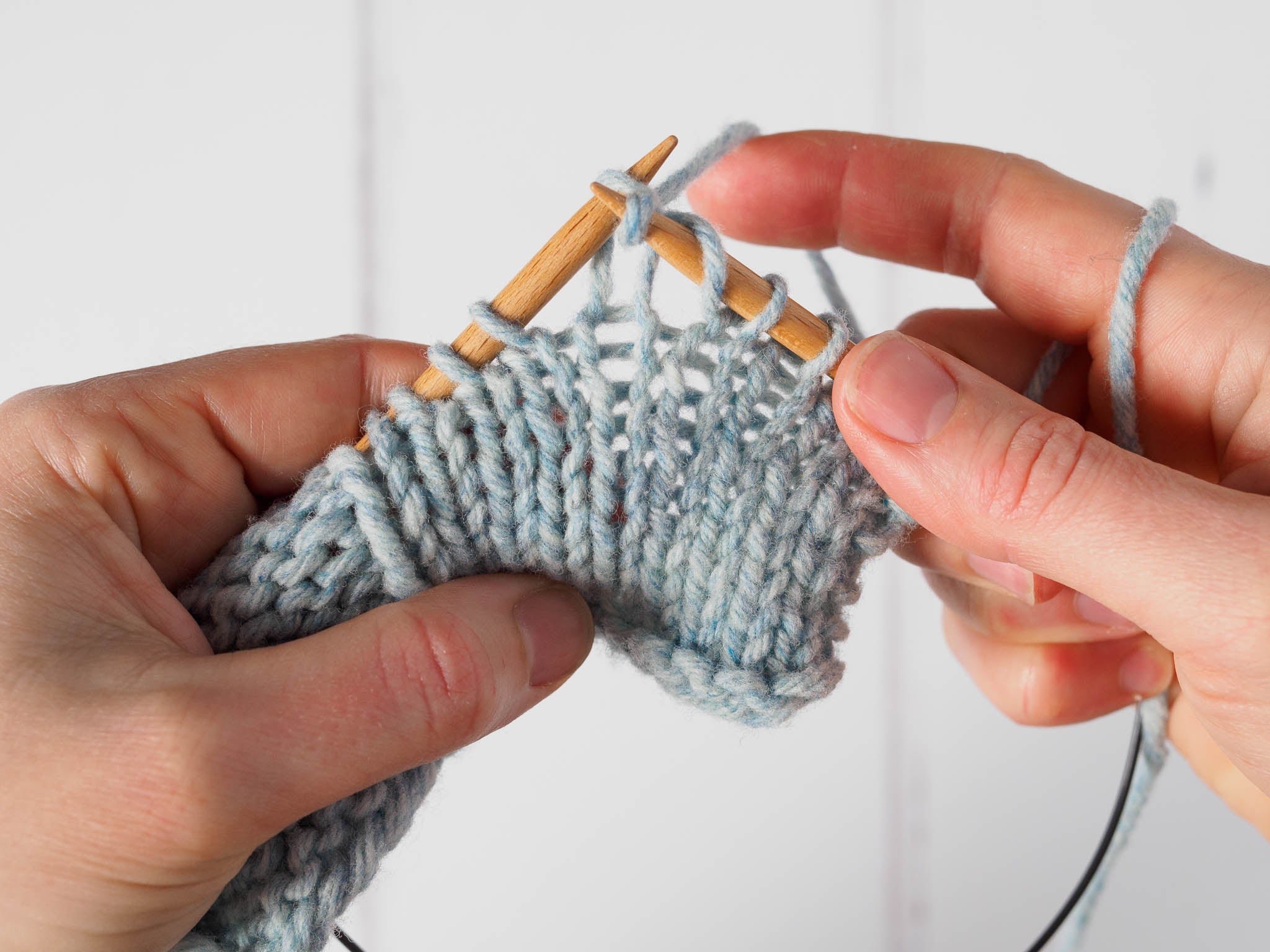 A small blue swatch showing a yarn over that's been created on the right needle, and the first stitch on the left needle is being knitted into.