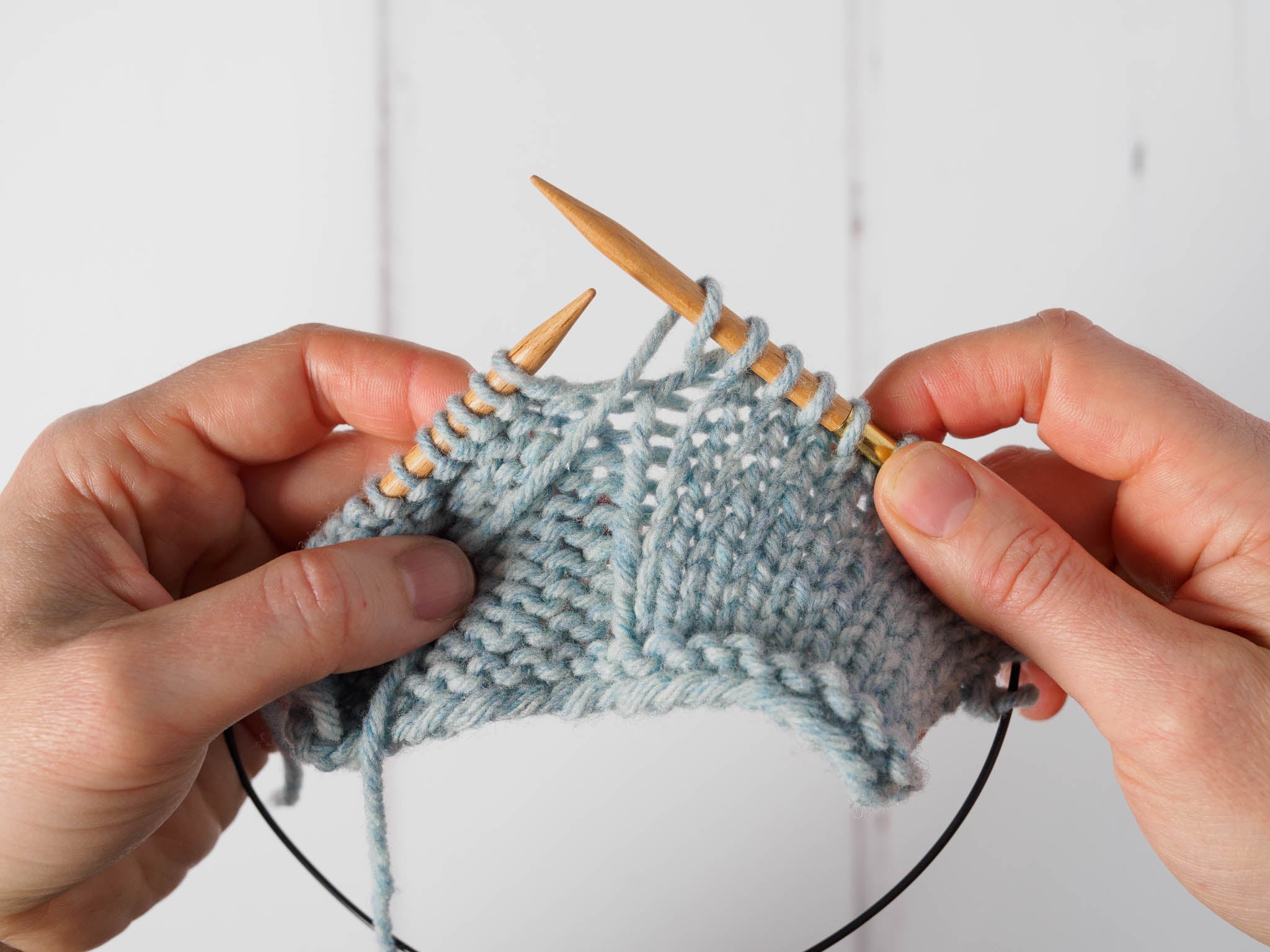 A small grey swatch with purl stitches to the left and column of knit stitches to the right. The yarn has been wrapped around the right needle to form a yarn over.