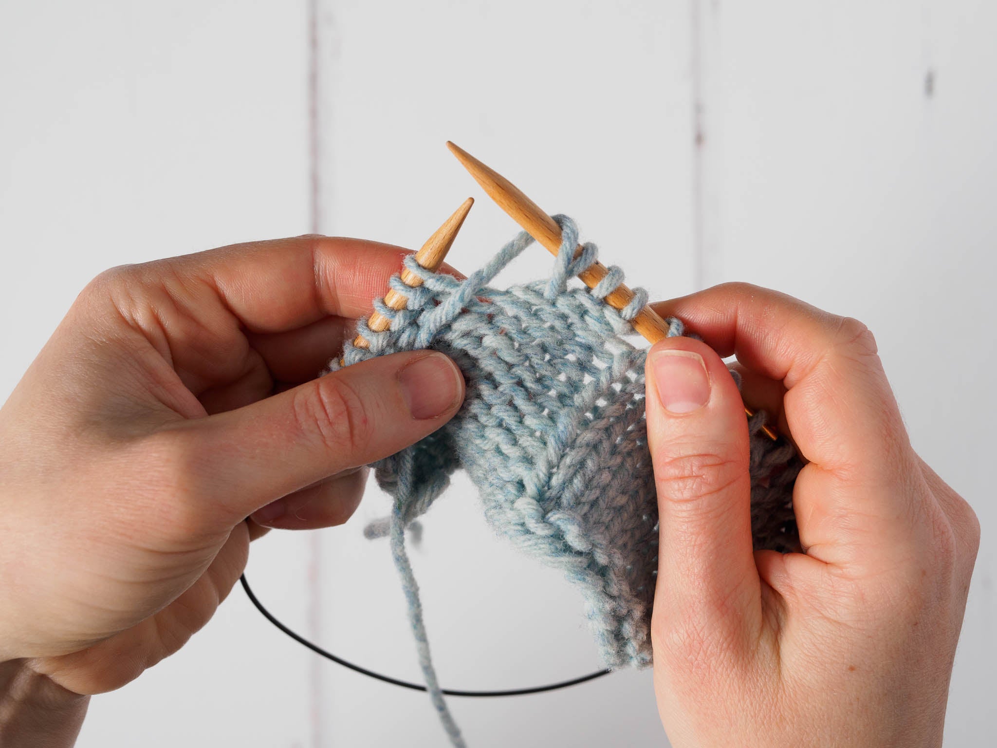 A small grey swatch where the working yarn between the needles has been wrapped around the right needle, from the front to the back. The yarn is now being held between the needles, at the front of the work.