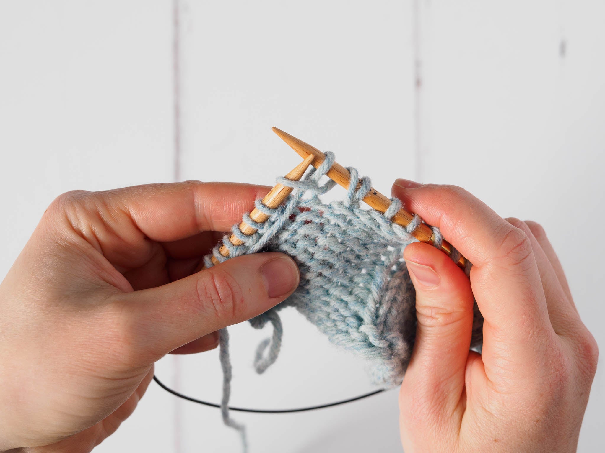 A small grey swatch where a yarn over has been formed on the right needle, and the next stitch is now being purled.