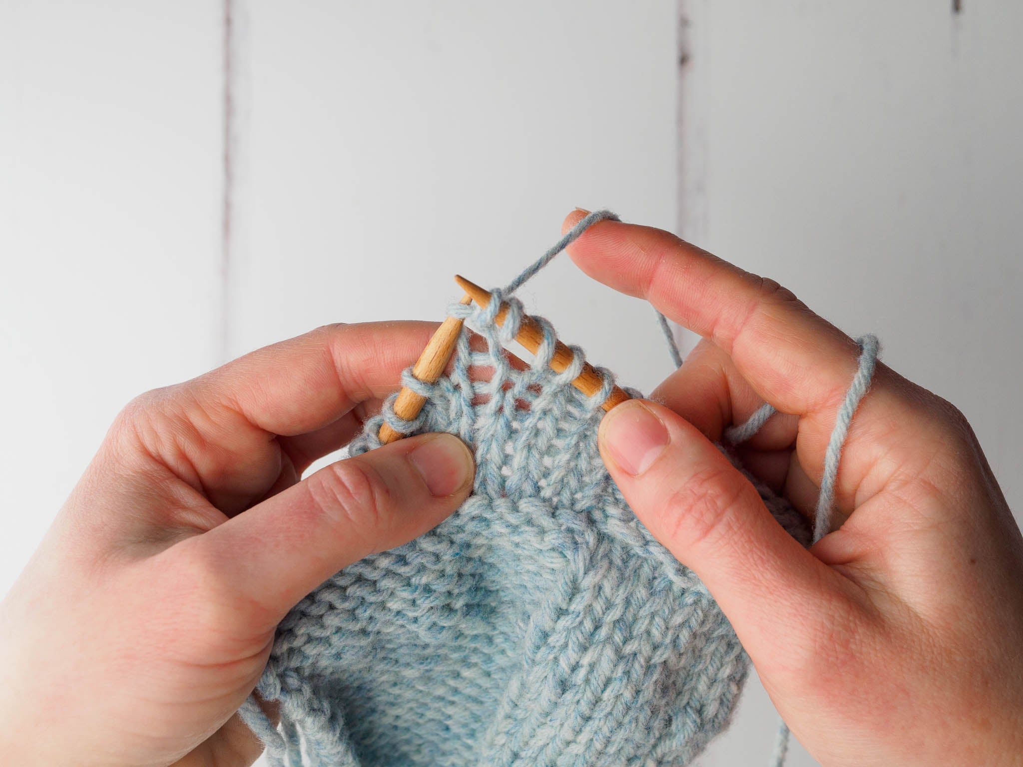 A small grey swatch with a double yarn over on the right needle. The next stitch on the left needle is being knitted.