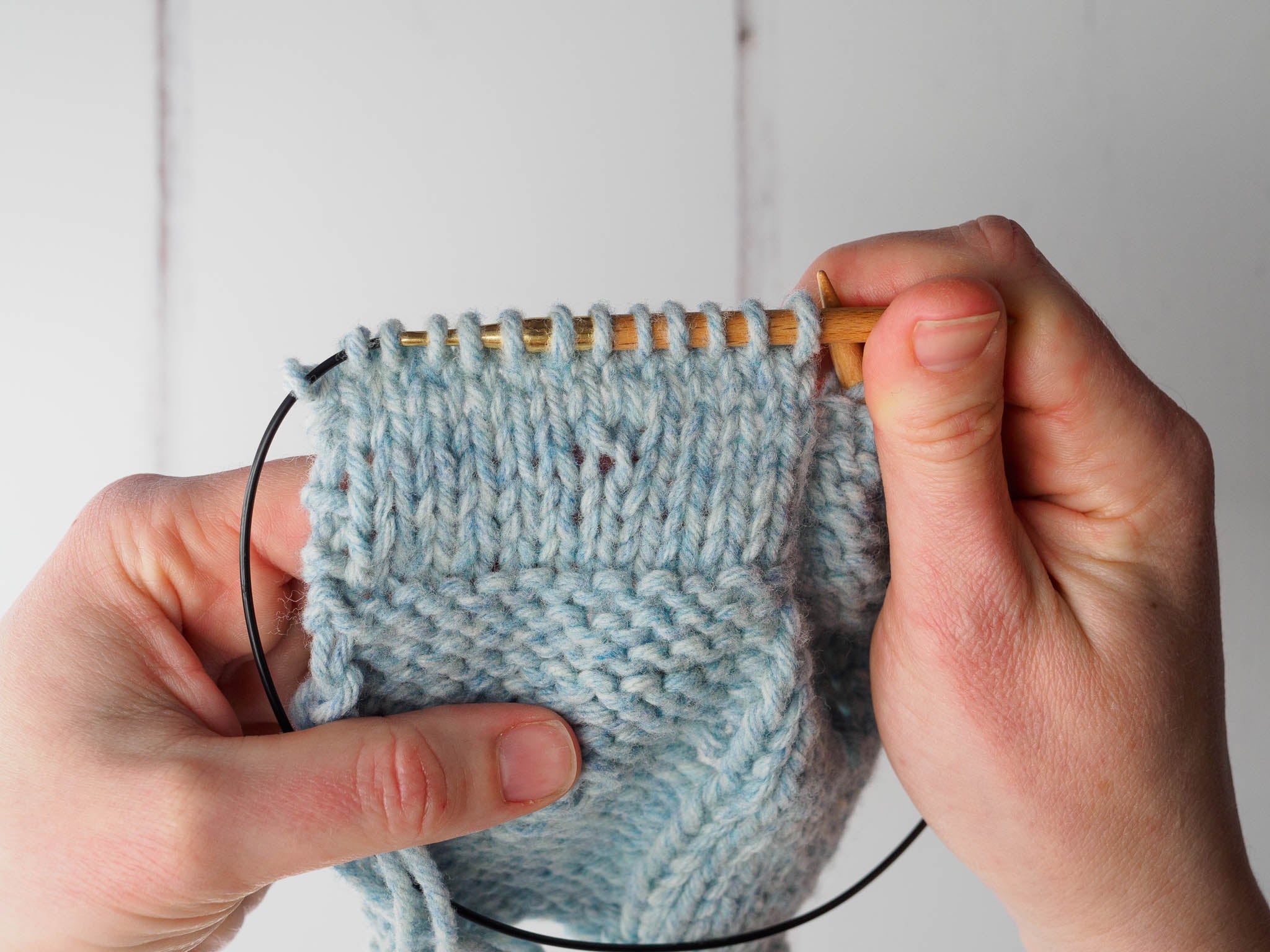 A swatch of pale blue knitting showing a closed yarn over in the centre of the fabric. The yarn over has been tightened to close the gap.