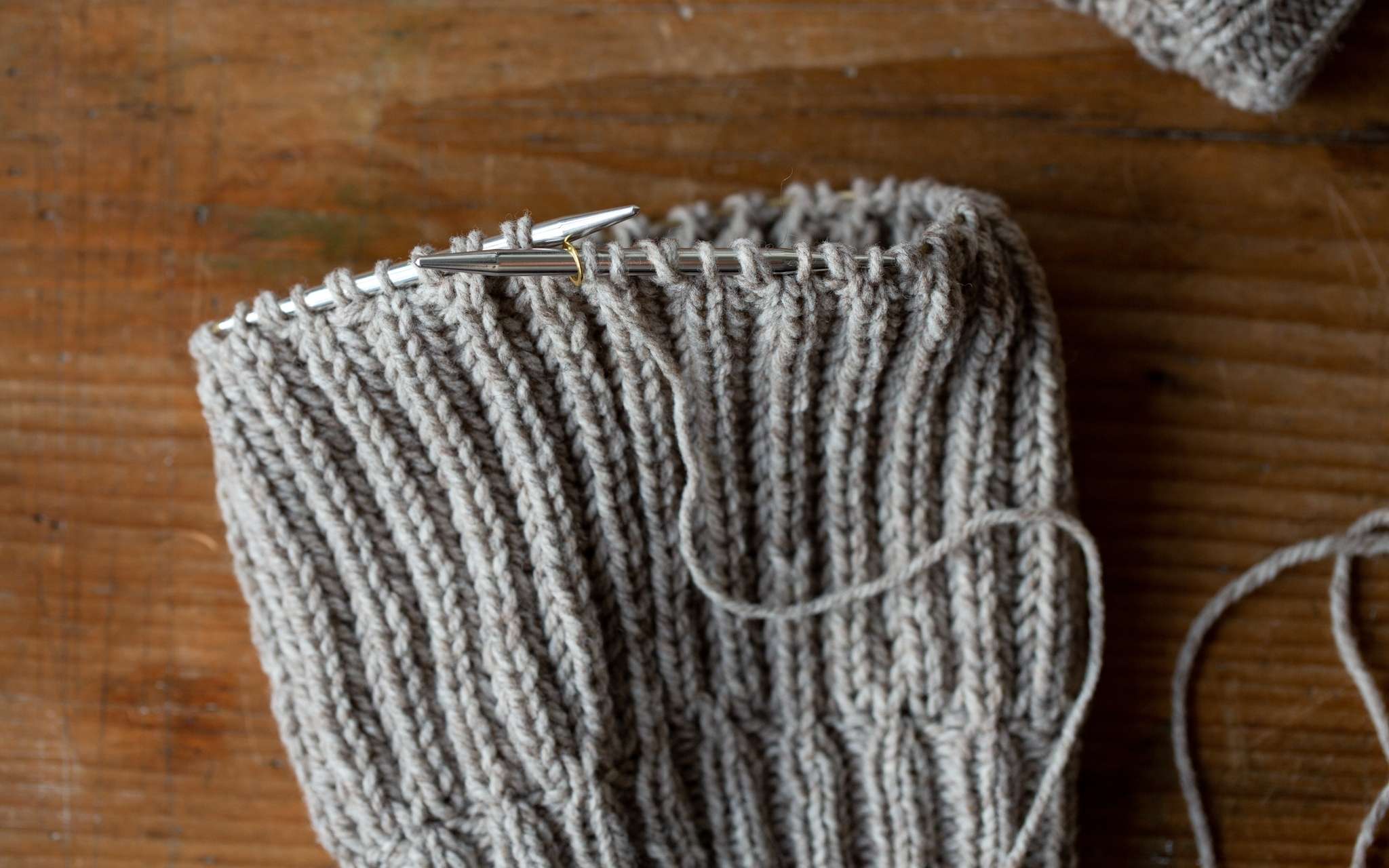 A hat in progress knitted in a brioche stitch, showing the yarn overs created nestled beside their corresponding stitches on the needle.