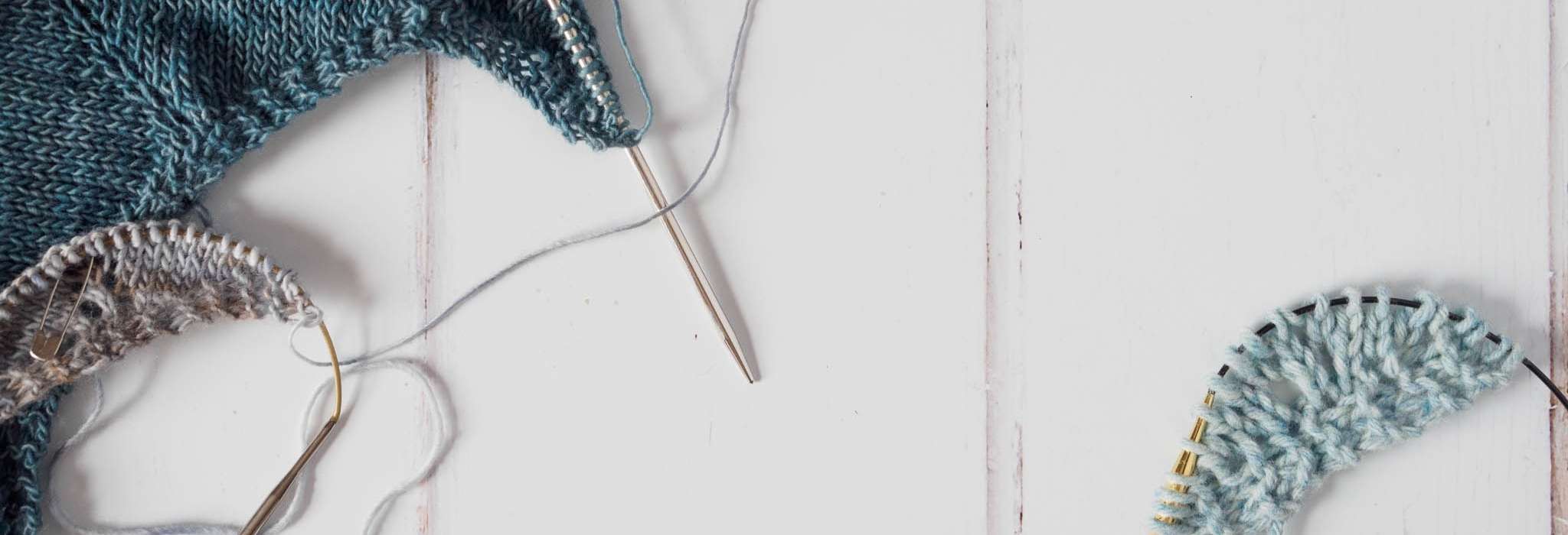 Light blue yarn and blue circular knitting needles on a wooden countertop.