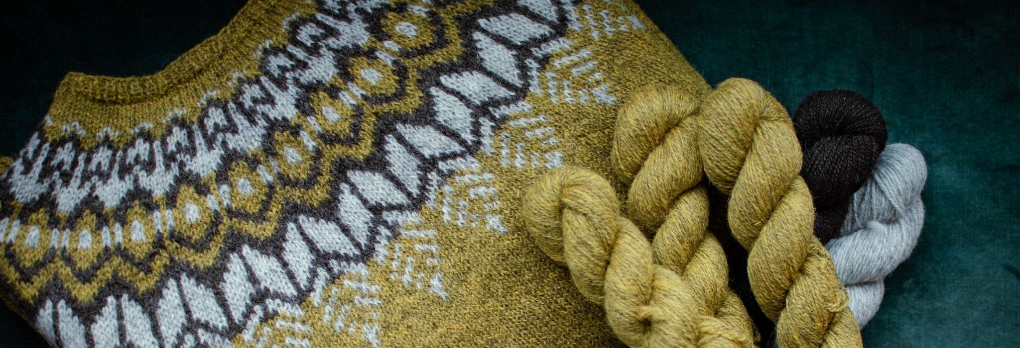 A close up of part of a colourwork yoke sweater in gold, brown and white. Some of the model's dark is visible over the top of the shoulder.