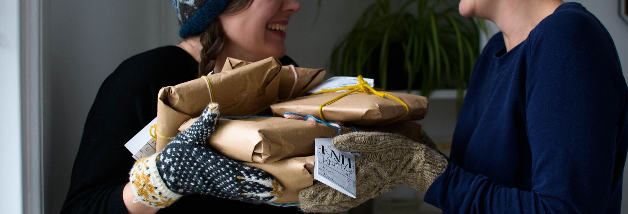 banner photo of two white people laughing and wearing mittens while holding a pile of wrapped gifts