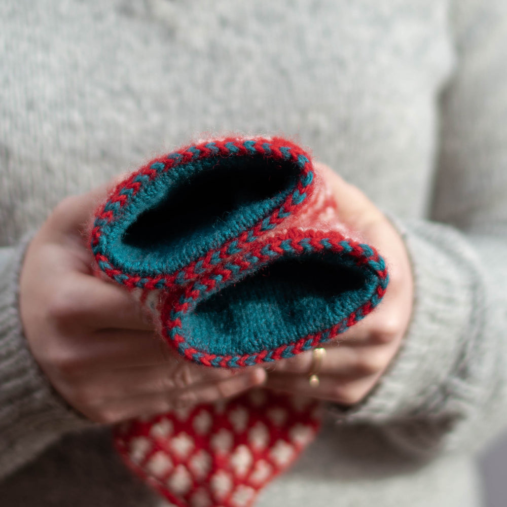 two white hands showing the camera a view of red and white mittens where we can see inside the mittens to see a blue lining