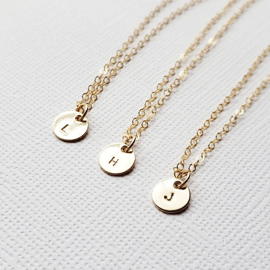 three gold small pendant necklaces with hand stamped letters in typewriter font shown in L H and j initials