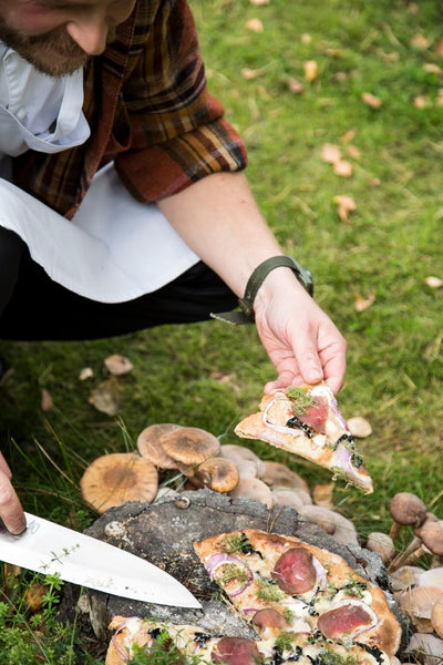 Picture of a Nordic bearded man slicing Nordic game pizza from the book Villiyrtit – hyvinvointia kotikulmilta (WSOY)