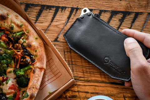 Renegade Zipper Wallet in Hand on table next to a pizza