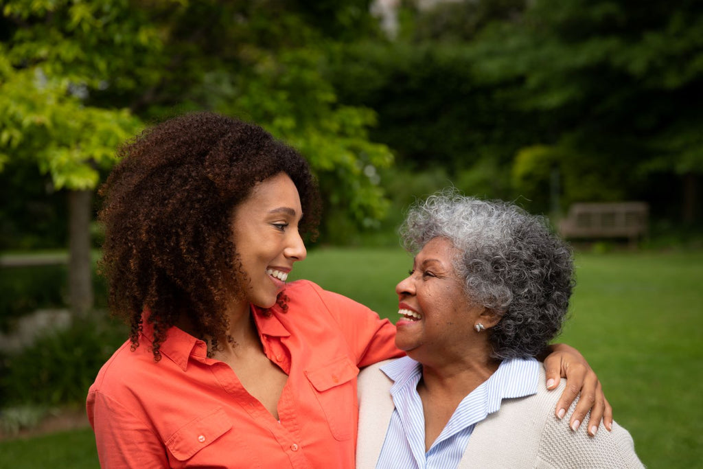 Elderly woman and adult daughter smile lovingly at each other while side hugging