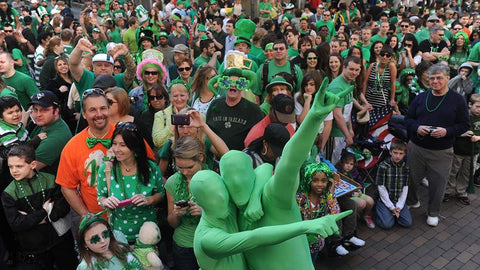 A crowd gathers during the St. Patrick's Day parade in Pittsburgh, PA. Two men in full body green morph suits are at the front of the crowd.