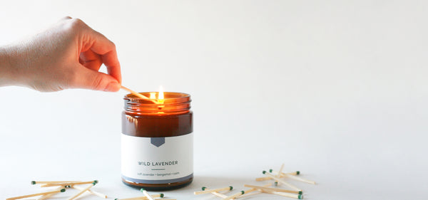 single hand lighting an amber glass jar soy candle, Wild Lavender - Vacant Wheel