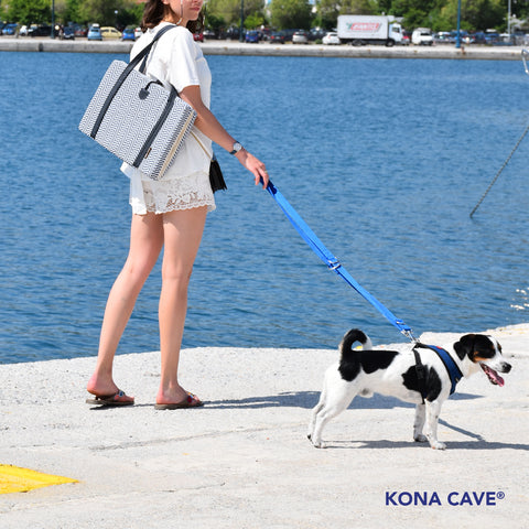 Das blau-weiße nautische KONA CAVE® Reise-Hundebett wird von einer jungen, modischen Hunde-Influencerin auf den griechischen Inseln getragen. Sie geht mit einem Jack Russell Terrier Hund spazieren.