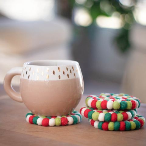 a tan ceramic mug rests on a red, white, and green wool coaster next to a stack of 3 more festive coasters