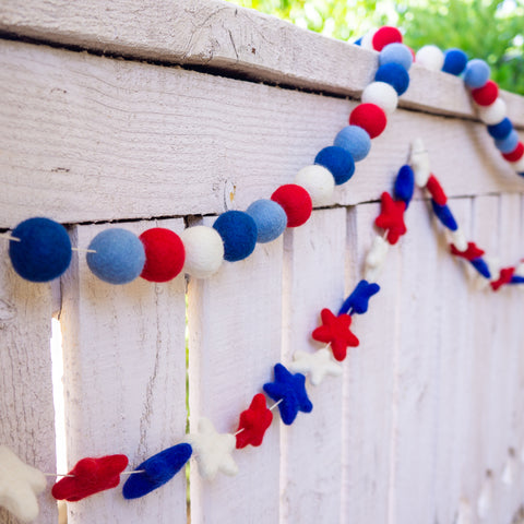 red white and blue beads and red white and blue star garland are draped over a white wood fence on a porch