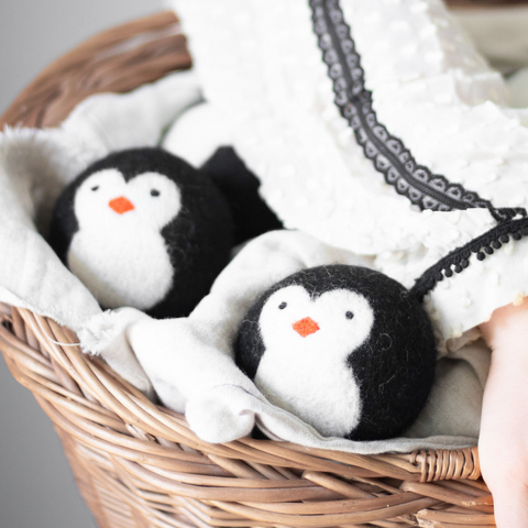 2 wool penguin dryer balls sit in white fabric in a wicker basket