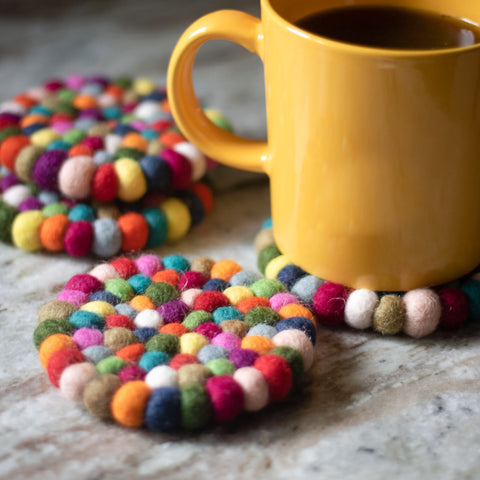 4 multicolor wool coasters on a countertop. A yellow mug is resting on one of the coasters.