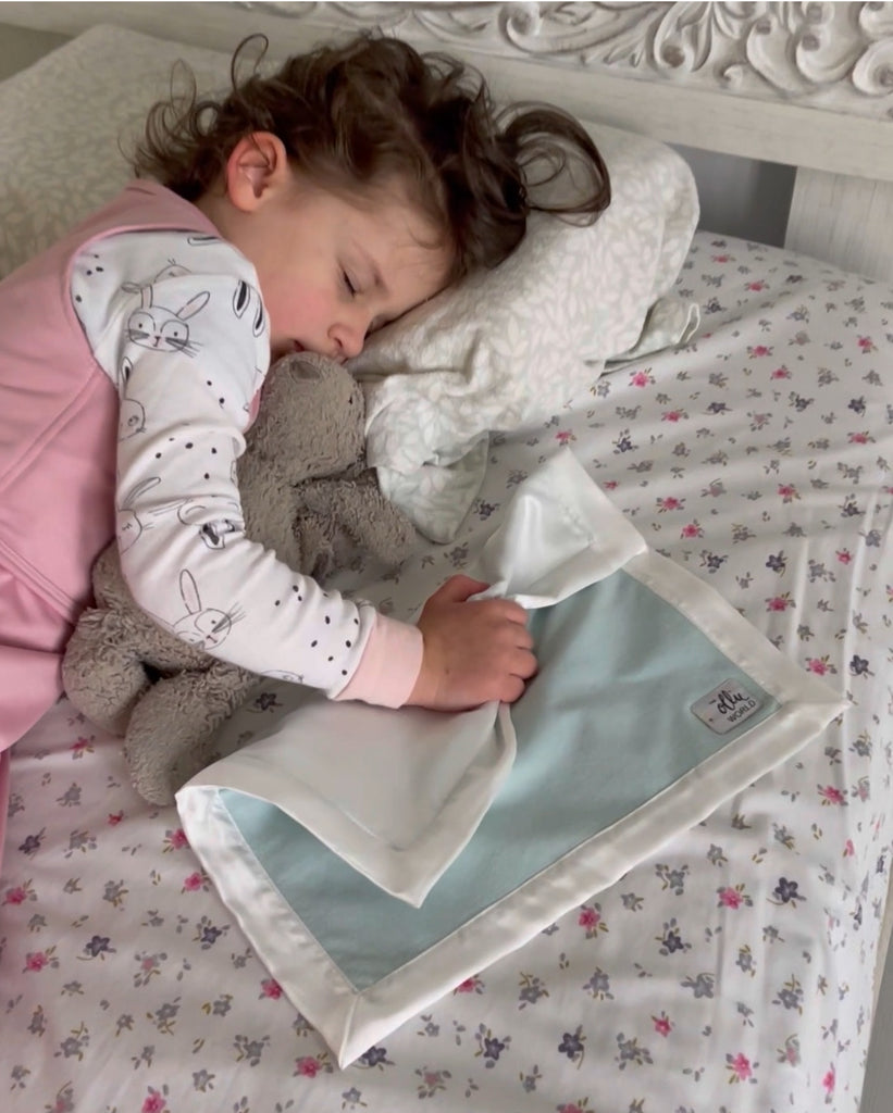 child sleeping in bed holding a light blue lovie with silky edge