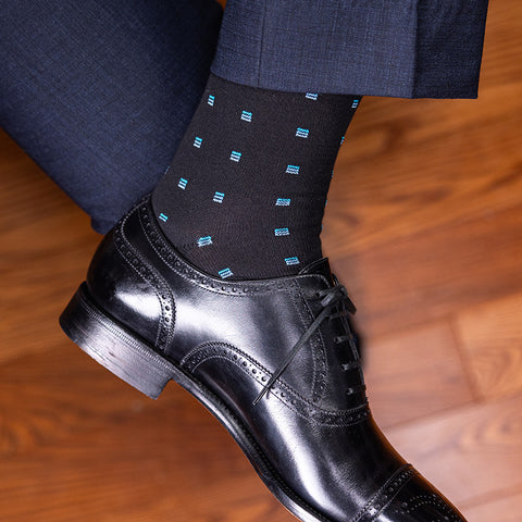 man crossing legs wearing black and blue patterned dress socks with black oxfords