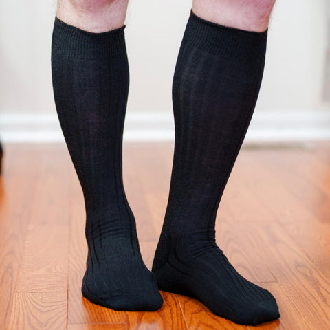 man wearing black wool over the calf dress socks standing on hardwood floor