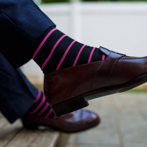 man crossing legs wearing black dress socks with bright pink horizontal stripes