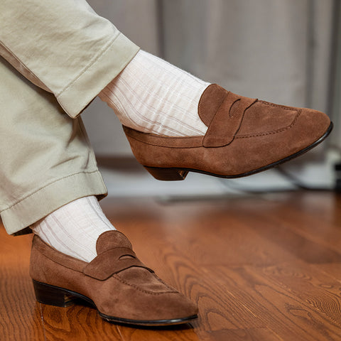 man crossing legs wearing cream dress socks and khaki chinos with brown suede penny loafers